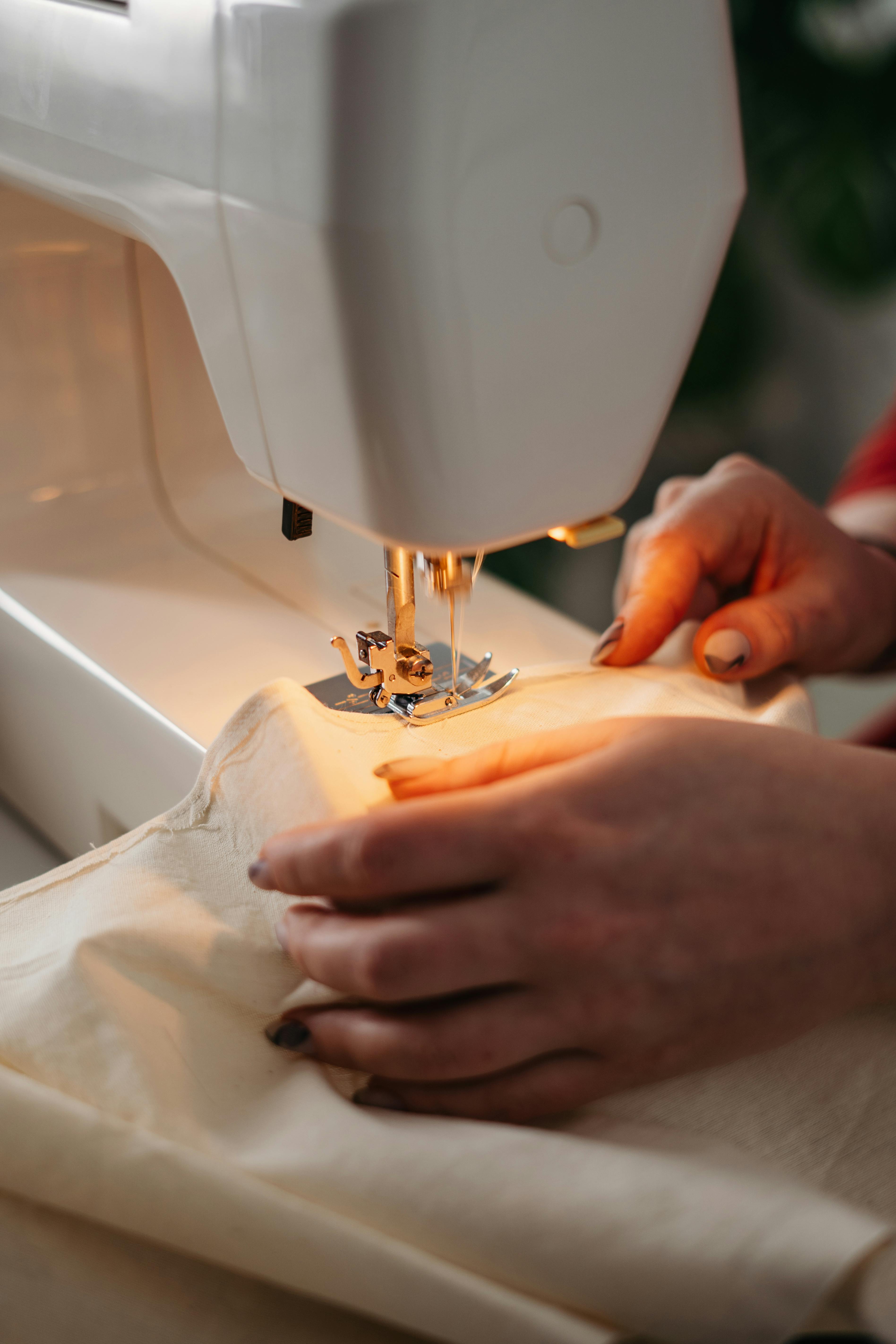 Hands guiding cream fabric through sewing machine — Italian artisan atelier